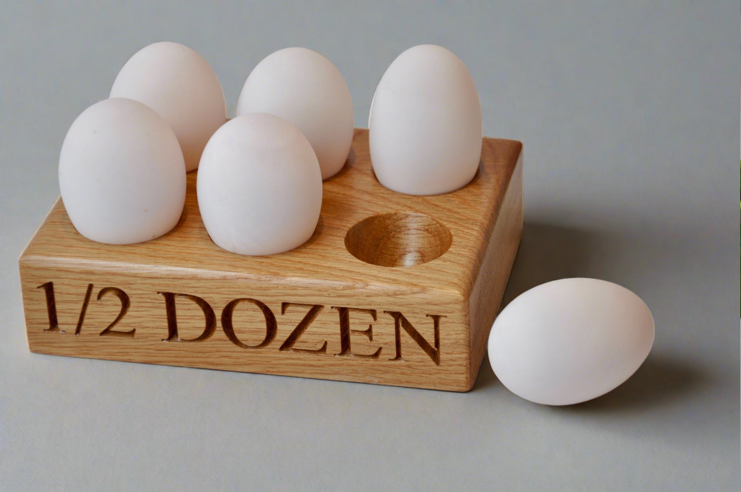 A solid oak egg holder with engraved text '1/2 DOZEN' on the front edge, displaying multiple eggs within its compartments, placed on a flat surface.